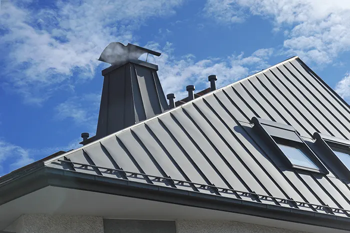 Dach mit Dachfenster und Schornstein eines Wohnhauses sind mit Aluminiumscharen verleidet.